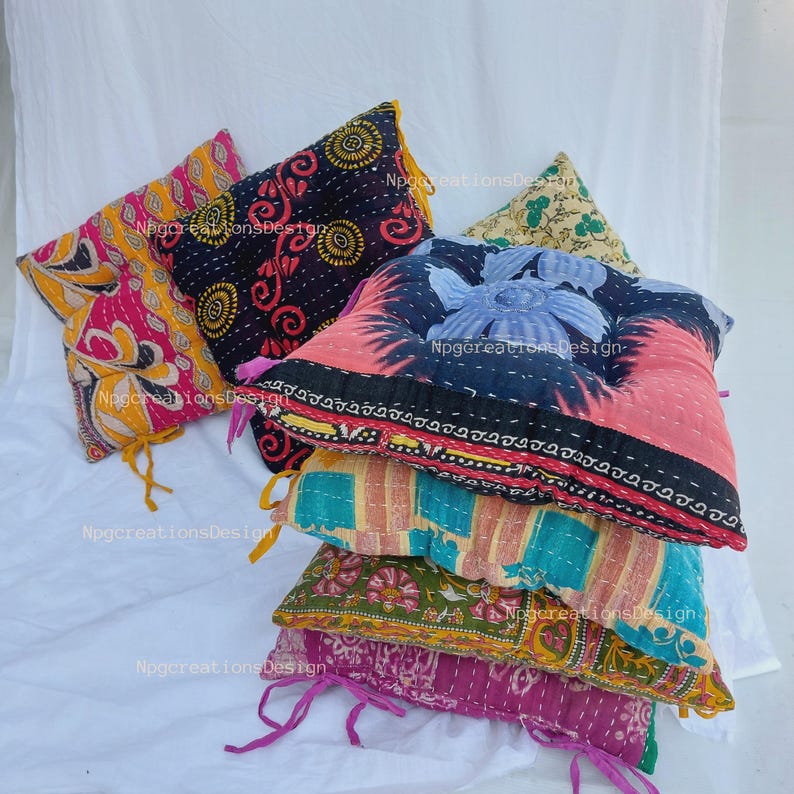 May include: A stack of five colourful, patterned, square throw cushions. The cushions are made of fabric scraps and are quilted. The cushions are arranged in a pyramid shape.
