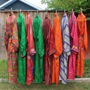 May include: A collection of nine long-sleeved robes hanging on a clothesline, featuring a variety of vibrant colors including green, orange, red, pink, and blue, with diverse patterns and textures visible across the fabric of each individual garment.