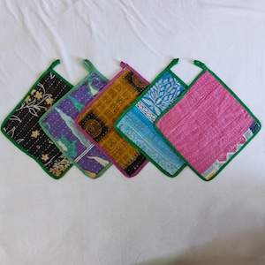 Può includere: Set di cinque presine imbottite colorate con bordino verde. Ogni presina presenta un motivo e una combinazione di colori diversi.