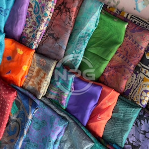 Könnte beinhalten: Eine Sammlung bunter Seidenschals mit verschiedenen Mustern und Designs. Die Schals sind in einem Stapel angeordnet, wobei sich einige überlappen. Die Farben umfassen Blau, Grün, Lila, Orange und Braun.