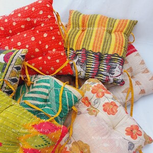 May include: A collection of colourful, square, quilted floor cushions with different patterns. The cushions are made of fabric with a variety of prints, including polka dots, stripes, and floral designs. The cushions have yellow ties.