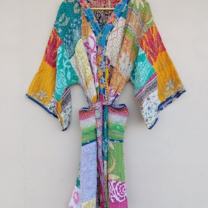 Op de afbeelding: Een patchwork kimono-jurk in verschillende kleuren, waaronder turquoise, geel, roze en wit. De jurk heeft een V-hals en lange mouwen. Het is gemaakt van een lichte stof en heeft een striksluiting in de taille.
