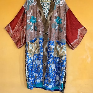 May include: A patchwork kimono-style robe with a brown, blue, and red floral design. The robe features a brown collar and trim, blue floral panels, and red sleeves with a patterned border. Two pockets are visible.