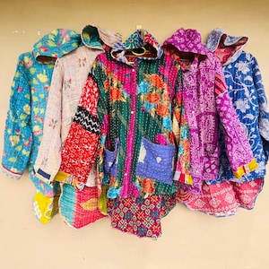 Puede incluir: Una colección de cinco chaquetas con capucha de manga larga que presentan vibrantes patrones de patchwork multicolor con estampados florales y geométricos. Cada chaqueta incluye un cierre de botones frontal y dos bolsillos de parche, con intrincadas costuras de estilo kantha en toda la tela.