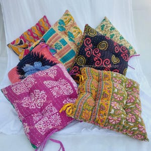 May include: A set of six colourful, patterned floor cushions. The cushions are made of fabric with a quilted design and have a square shape. The cushions are in various colours, including pink, purple, blue, green, yellow, and black.