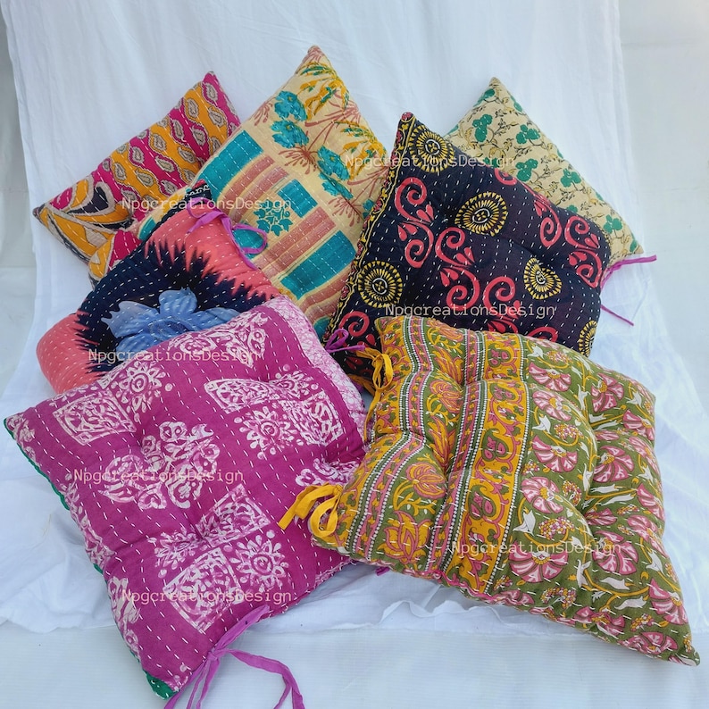 May include: A set of six colourful, patterned floor cushions. The cushions are made of fabric with a quilted design and have a square shape. The cushions are in various colours, including pink, purple, blue, green, yellow, and black.
