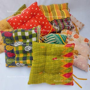May include: A set of six colourful, square, quilted floor cushions. The cushions are made from a variety of fabrics, including floral prints, stripes, and polka dots. The cushions are tied together with yellow string.