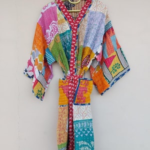 May include: A colorful patchwork kimono robe with a tie belt, hanging on a yellow hanger. The robe features a variety of fabric patterns in shades of orange, pink, green, blue, and yellow. The robe is made of a soft, lightweight material.