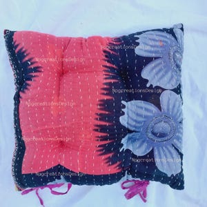 May include: A red and black floral patterned cushion with a quilted design and pink ties. The cushion is made from recycled fabric and has a unique, handmade look.