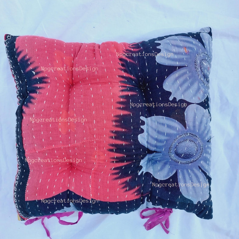May include: A red and black floral patterned cushion with a quilted design and pink ties. The cushion is made from recycled fabric and has a unique, handmade look.