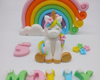 May include: A white unicorn figurine with a gold horn and colorful mane, positioned in front of a multi-colored rainbow arch. The set includes a pink number five, small pastel flowers, and the name MOLLY spelled out in colorful block letters.