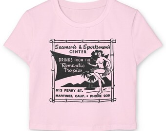 Peut inclure: Un crop top rose clair avec un motif noir et blanc. Le motif comprend le texte "Seamen's & Sportsmen's CENTER" et "DRINKS FROM THE Romantic Tropics". Une illustration vintage d'une femme dansant est également présente.