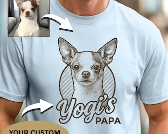 Op de afbeelding: Lichtblauw T-shirt met een gedetailleerde illustratie van een Chihuahua-hond in een cirkelvormige lijst. De tekst "Yogi's PAPA" staat onder de afbeelding van de hond. Een kleine foto van de hond staat in de linkerbovenhoek. Het shirt heeft een ronde hals.