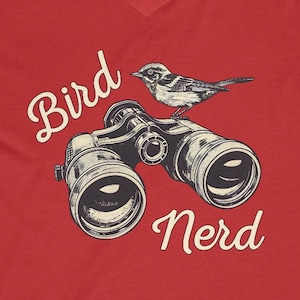 May include: Red V-neck t-shirt with a bird perched on a pair of binoculars and the text "Bird Nerd".