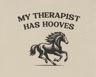 May include: A beige t-shirt with the text "MY THERAPIST HAS HOOVES" and a black silhouette of a horse running.