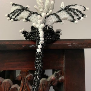 May include: A black and white rubber band dragon with a long tail, sitting on a wooden stand. The dragon has wings and a spiky head.