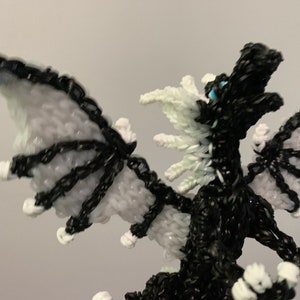 May include: A black and white dragon made of rubber bands. The dragon has white wings and a white mane. The dragon's eyes are blue.