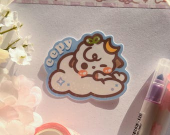 May include: A white sticker featuring a cartoon dog sleeping on a blue cloud. The dog has a green bow and a crescent moon on its head. The sticker reads "eeepy" in a bubbly font.