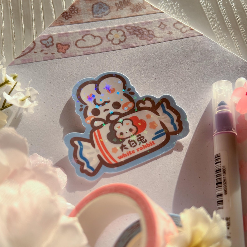 Puede incluir: Una pegatina azul y blanca con un conejo blanco de dibujos animados sosteniendo una barra de caramelo. La barra de caramelo est&aacute; envuelta en papel de aluminio y tiene el texto "White Rabbit" y caracteres chinos.