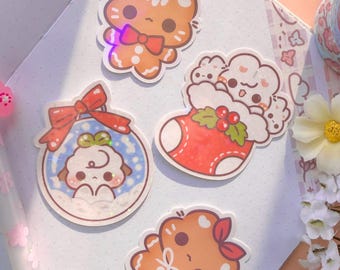 May include: A collection of colorful, whimsical stickers featuring cute cartoon characters. Designs include a gingerbread man with a bow tie, a sheep in a snow globe, and a character in a Christmas stocking. The stickers are on a white background.