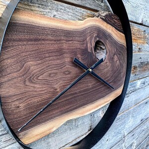 Peut inclure: Une horloge en bois avec un cadre en métal noir et des aiguilles noires. Le cadran de l'horloge est fait d'une tranche de bois naturelle avec un trou de nœud au centre.