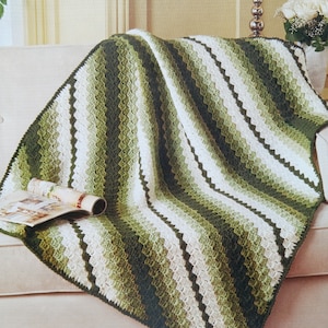 May include: A crocheted throw blanket with a diagonal striped pattern in shades of green and white. The blanket is draped over a white couch.