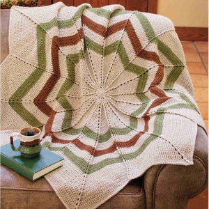 May include: A crocheted throw blanket with a starburst pattern in shades of brown, green, and white. The blanket is draped over a brown leather armchair.