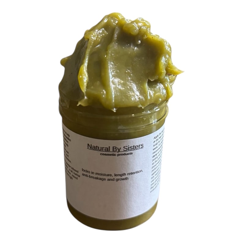 Pode incluir: Um frasco de produto cosm&eacute;tico Natural By Sisters. O frasco cont&eacute;m uma subst&acirc;ncia espessa verde-oliva. O r&oacute;tulo diz "locks in moisture, length retention, anti-breakage and growth."