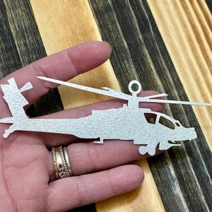 May include: A white metal silhouette of a helicopter, with a textured surface, is held in a person's hand.