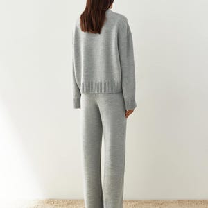 May include: A gray knitted sweater and matching pants set. The sweater has a relaxed fit and a ribbed hem. The pants have a wide leg and a ribbed cuff.