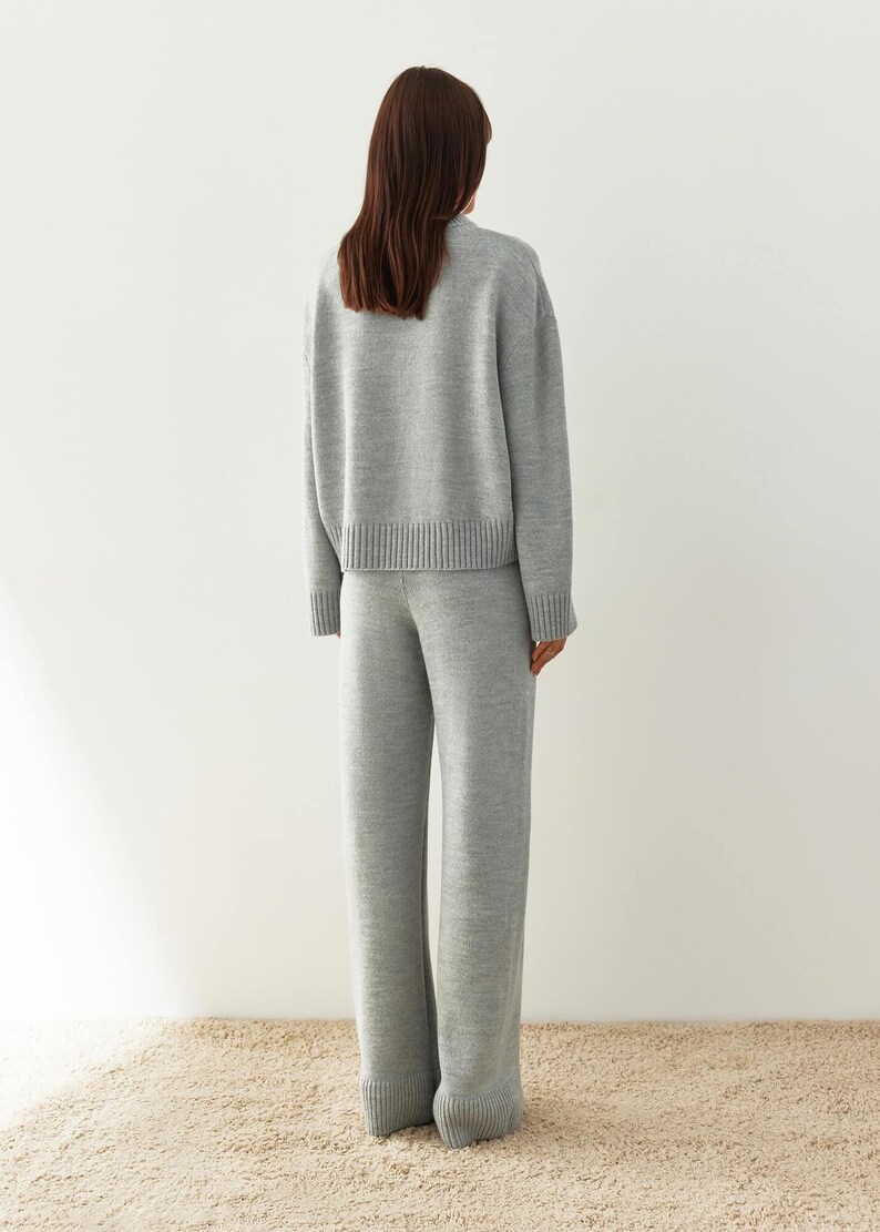 May include: A gray knitted sweater and matching pants set. The sweater has a relaxed fit and a ribbed hem. The pants have a wide leg and a ribbed cuff.