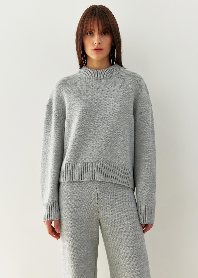 May include: A gray knitted sweater and matching pants set. The sweater has a round neckline and long sleeves. The pants are wide-legged and cropped.