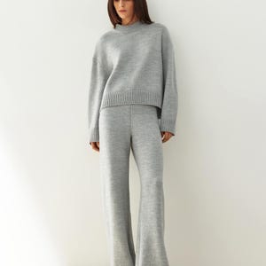 May include: A gray knitted sweater and matching wide-leg pants. The sweater has a round neckline and a cropped length. The pants have a wide leg and a relaxed fit.