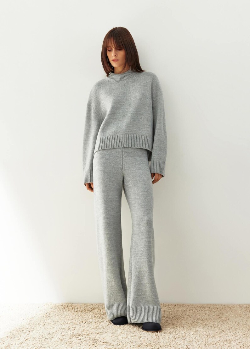 May include: A gray knitted sweater and matching wide-leg pants. The sweater has a round neckline and a cropped length. The pants have a wide leg and a relaxed fit.