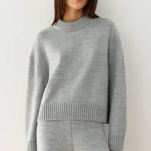 May include: A gray knitted sweater and matching pants set. The sweater has a round neckline and long sleeves. The pants have a relaxed fit.