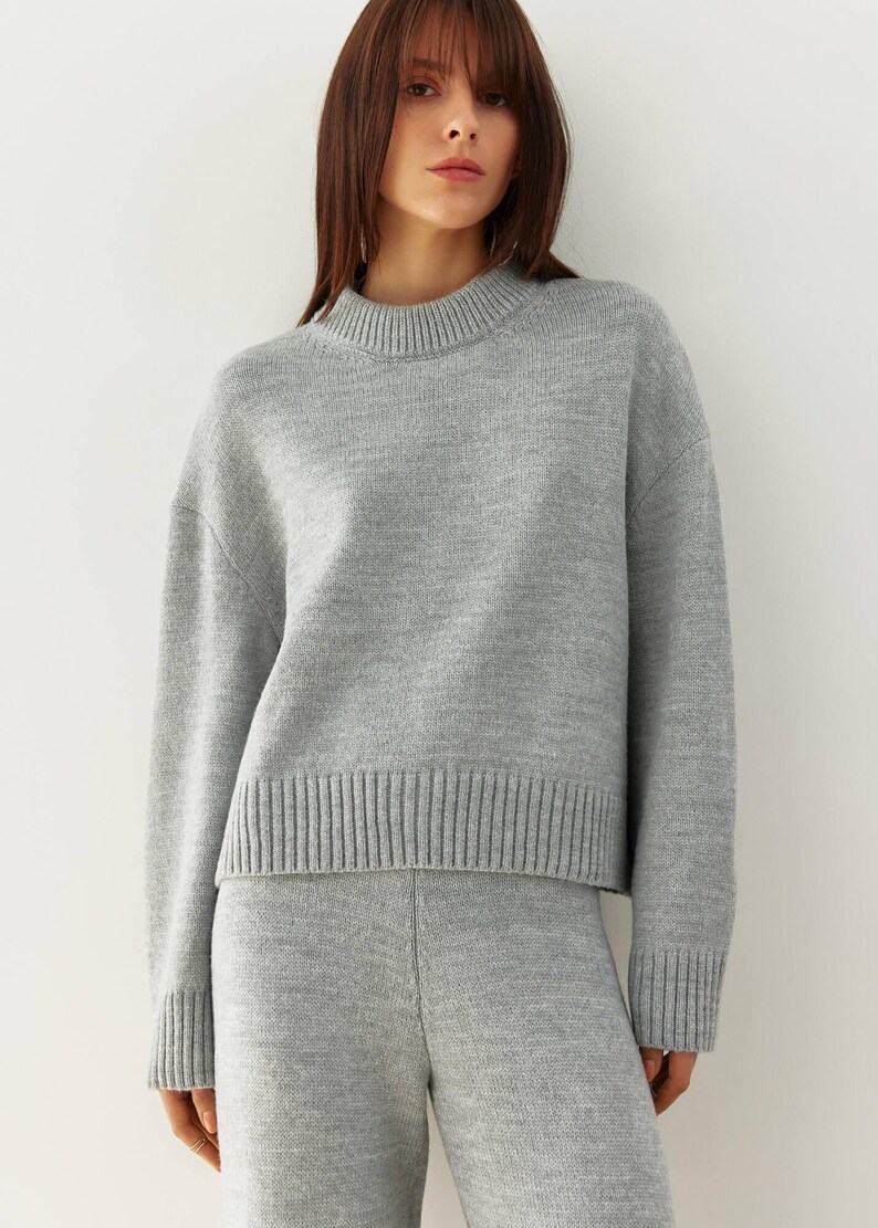 May include: A gray knitted sweater and matching pants set. The sweater has a round neckline and long sleeves. The pants have a relaxed fit.