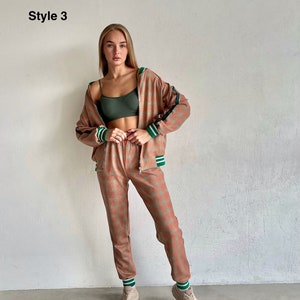 May include: A woman is wearing a pink and green patterned tracksuit with a green and white striped trim. The tracksuit includes a zip-up jacket and matching pants. She is wearing white sneakers.