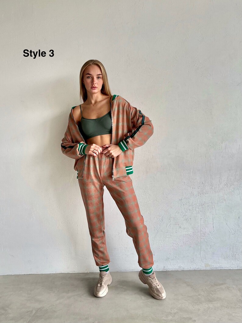 May include: A woman is wearing a pink and green patterned tracksuit with a green and white striped trim. The tracksuit includes a zip-up jacket and matching pants. She is wearing white sneakers.