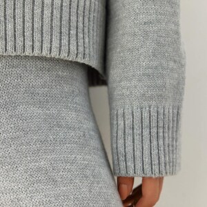 May include: A gray knitted sweater and skirt set. The sweater has a ribbed texture and the skirt is a simple, straight cut.