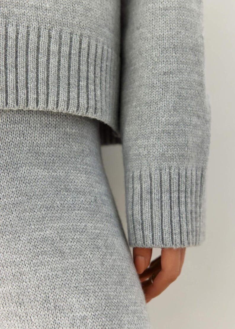 May include: A gray knitted sweater and skirt set. The sweater has a ribbed texture and the skirt is a simple, straight cut.
