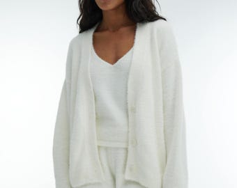 May include: A white fuzzy cardigan with a matching white fuzzy tank top and shorts. The cardigan has a button closure and a v-neck.