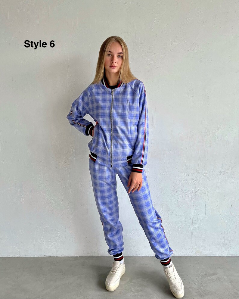 May include: A blue and white plaid tracksuit with red and black trim. The jacket has a zipper closure and the pants have a drawstring waist. The model is wearing white sneakers.