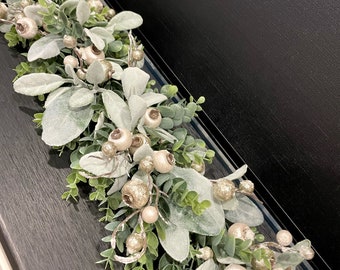 Könnte beinhalten: Eine dekorative Girlande mit gefrosteten grünen Lammohrblättern, kleinen grünen Eukalyptuszweigen und Clustern aus champagnerfarbenen Beeren mit Glitzer-Finish. Ein kleiner runder weißer Aufkleber mit dem Text Wreath Solution ist zu sehen.