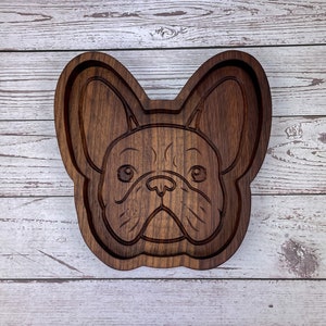 May include: A wooden tray shaped like a French Bulldog's face. The tray is dark brown and has a detailed carving of the dog's features.