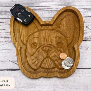 May include: A wooden tray shaped like a French Bulldog's face. The tray is 8 inches by 8 inches and is made of oak. It has a natural wood finish and is perfect for holding small items like keys, coins, or jewelry.