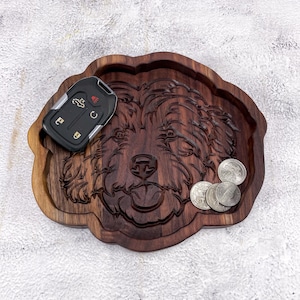 May include: A wooden tray carved in the shape of a dog's head. The tray is dark brown and has a natural wood finish. There are a few silver coins in the tray and a car key.