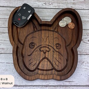 May include: A wooden tray shaped like a French Bulldog, with a carved design of the dog's face. The tray is 8 inches by 8 inches and is made of walnut wood. The tray has a small indentation on the top for holding small items, such as keys or coins.