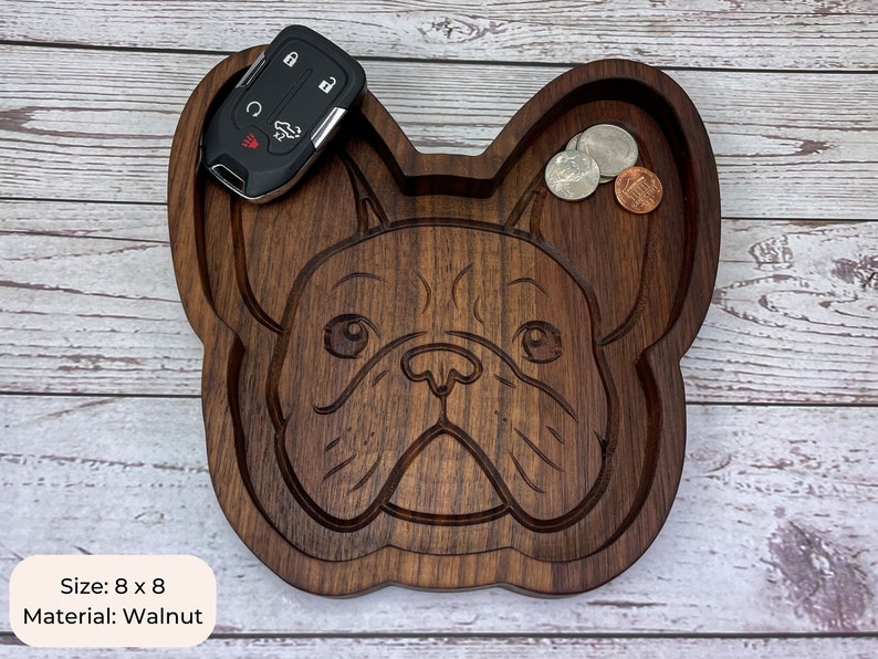 May include: A wooden tray shaped like a French Bulldog, with a carved design of the dog's face. The tray is 8 inches by 8 inches and is made of walnut wood. The tray has a small indentation on the top for holding small items, such as keys or coins.