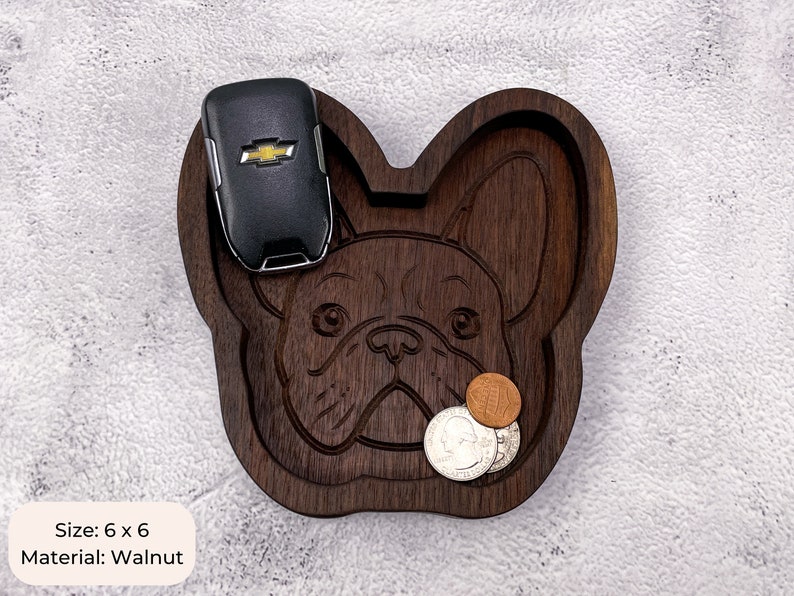 May include: A wooden tray shaped like a French Bulldog, with a black car key and coins inside. The tray is 6 inches by 6 inches and made of walnut wood. Size: 6 x 6 Material: Walnut