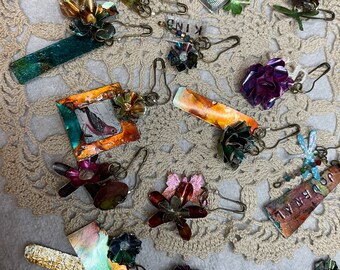 May include: A collection of colorful metal charms with various designs, including flowers, birds, and abstract patterns. Each charm is attached to a safety pin, making them perfect for adding a touch of whimsy to clothing, bags, or other accessories.